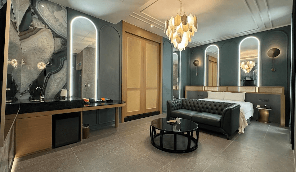 【草屯住宿】山月景緻旅館的雙人房，設有皮質沙發與圓形茶几、金屬感吊燈與對稱鏡面牆設計，牆面採用墨藍與米色對比配色，空間典雅時尚，適合浪漫或輕奢住宿體驗。