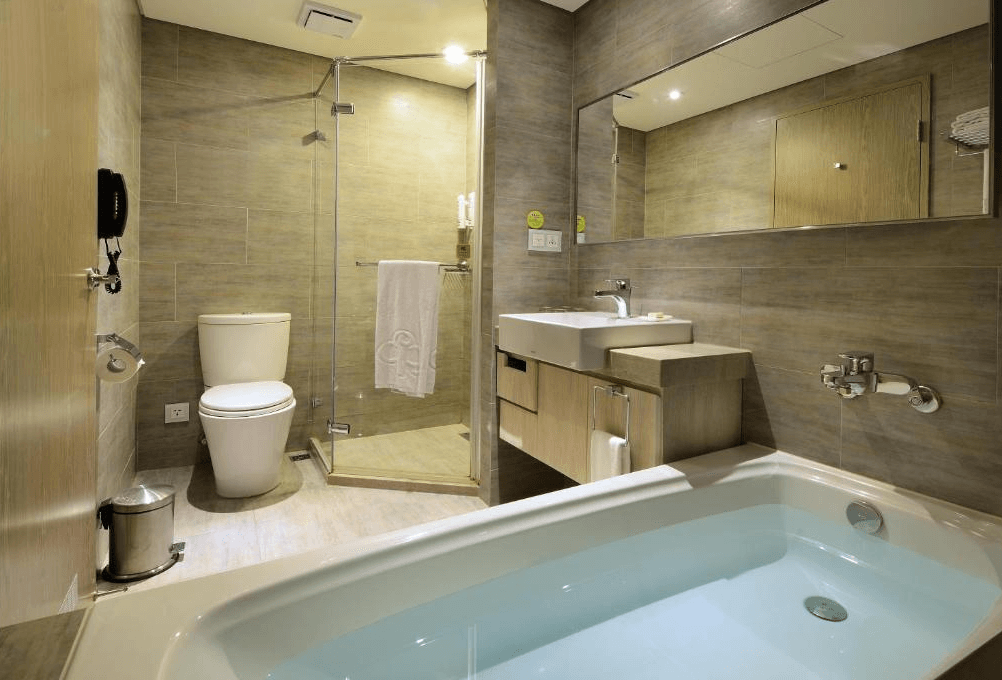 【蘆洲住宿】成旅晶贊飯店-蘆洲館的衛浴空間，設有乾濕分離淋浴間與獨立浴缸，牆面採用木紋磁磚，搭配大面鏡與收納洗手台，整體清潔明亮。