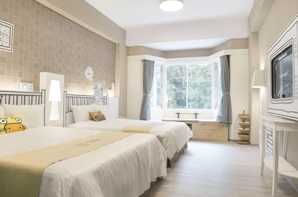 【杉林溪住宿】明山森林會舘的童趣風格雙床房，以插畫牆面與可愛抱枕增添活潑氛圍，設有大面窗景與日式窗台座位，採光明亮適合親子入住。
