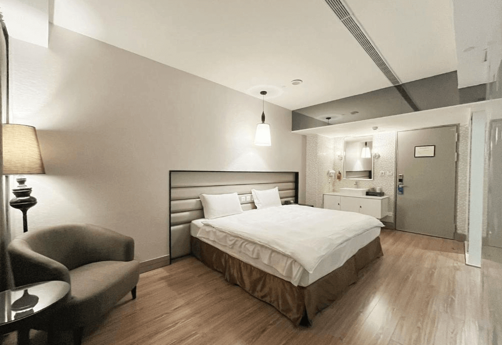 【一中街住宿】星漾商旅一中館的雙人房，設有一張雙人床，柔和燈光與木地板營造溫暖氛圍，房內配有舒適單人沙發與邊桌，整體空間寬敞清爽。