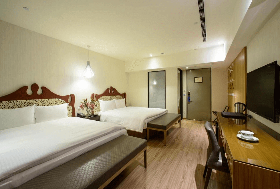 【一中街住宿】星漾商旅一中館的四人房，配有兩張雙人床與典型雕花床頭板，房內擺放花卉裝飾、長凳與書桌，並提供熱水壺與茶具設施，適合家庭旅遊入住。