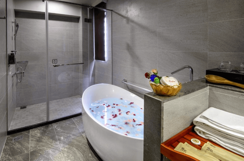【一中街住宿】星漾商旅一中館的浴室，配有獨立圓形浴缸與乾濕分離淋浴間，石材牆面與地板提升整體質感，備有毛巾、盥洗用品與精緻小籃子，泡澡空間寬敞愜意。