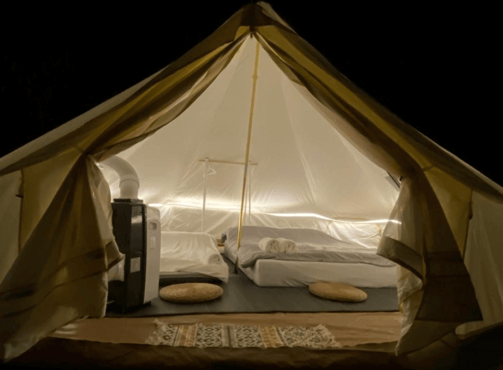 【龍潭住宿】晃晃印地安帳篷露營區，帳篷內部設有兩張低床墊與圓坐墊，採用柔和燈光營造溫馨舒適的睡眠空間。內部配有吊衣架與移動冷氣機，讓露營體驗更貼近飯店式舒適，適合家庭或情侶共宿。