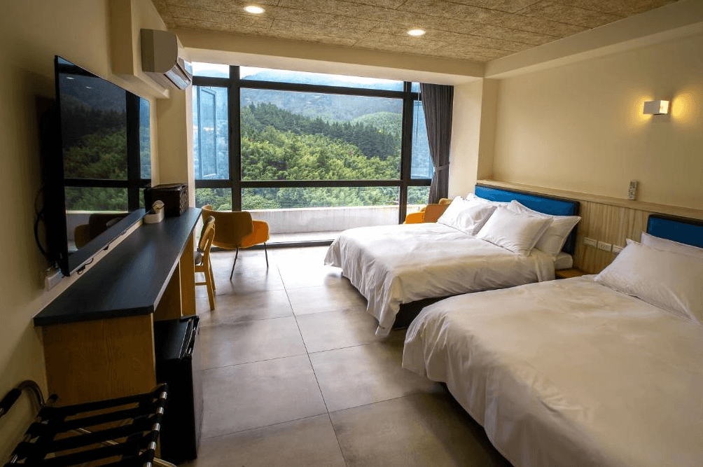 【杉林溪住宿】晨煦行旅具有大片落地窗與山景的雙人雙床客房，室內配有現代簡約風格傢俱、電視與工作桌。