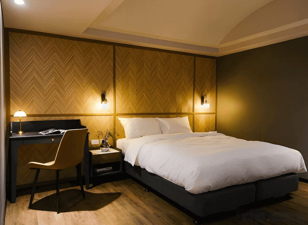 【三重住宿】柜富旅店的雙人房空間，床頭板為人字拼設計，搭配昏黃壁燈與簡約黑色書桌，營造出高雅又沉穩的住宿氛圍，適合情侶或商務旅客入住。