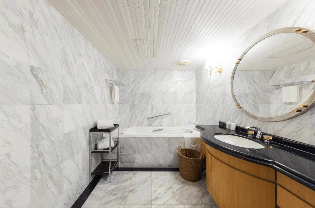 【龍潭住宿】桃園高爾夫俱樂部 ‧ 悅華大酒店，白色大理石鋪設的典雅浴室，配有浴缸與洗手台，搭配大圓鏡與溫暖燈光，呈現高級飯店質感。備品整齊擺放於層架上，整體空間明亮清爽，適合享受放鬆泡澡時光。