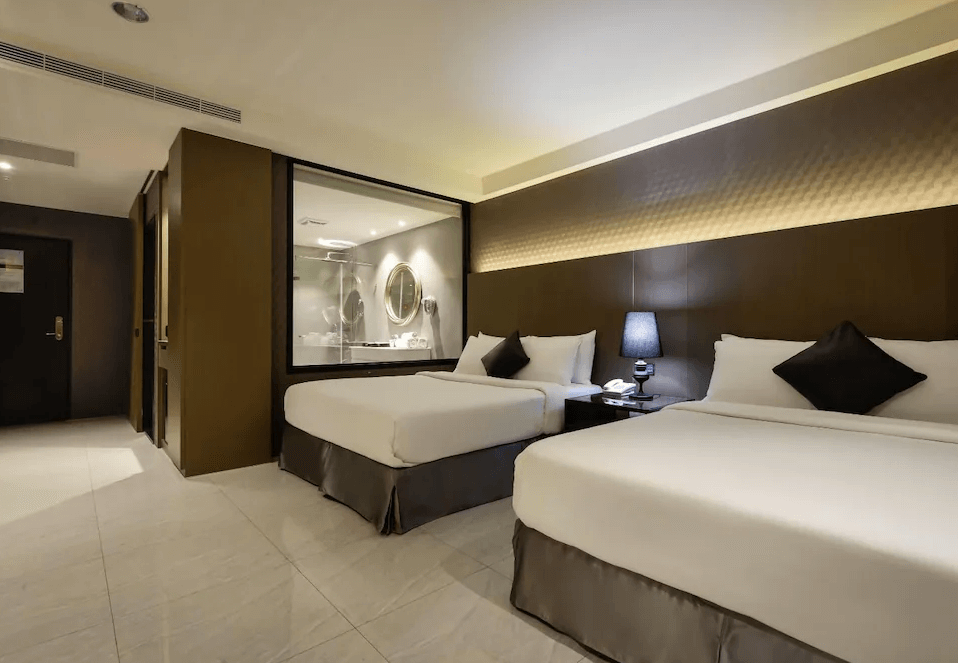 【草屯住宿】沐悅時尚精品旅館的雙床房型，設有兩張大床與對稱床頭燈，房內以深棕與米色系為主色調，浴室外觀以透明玻璃隔間設計，營造開放感與現代感兼具的住宿空間。