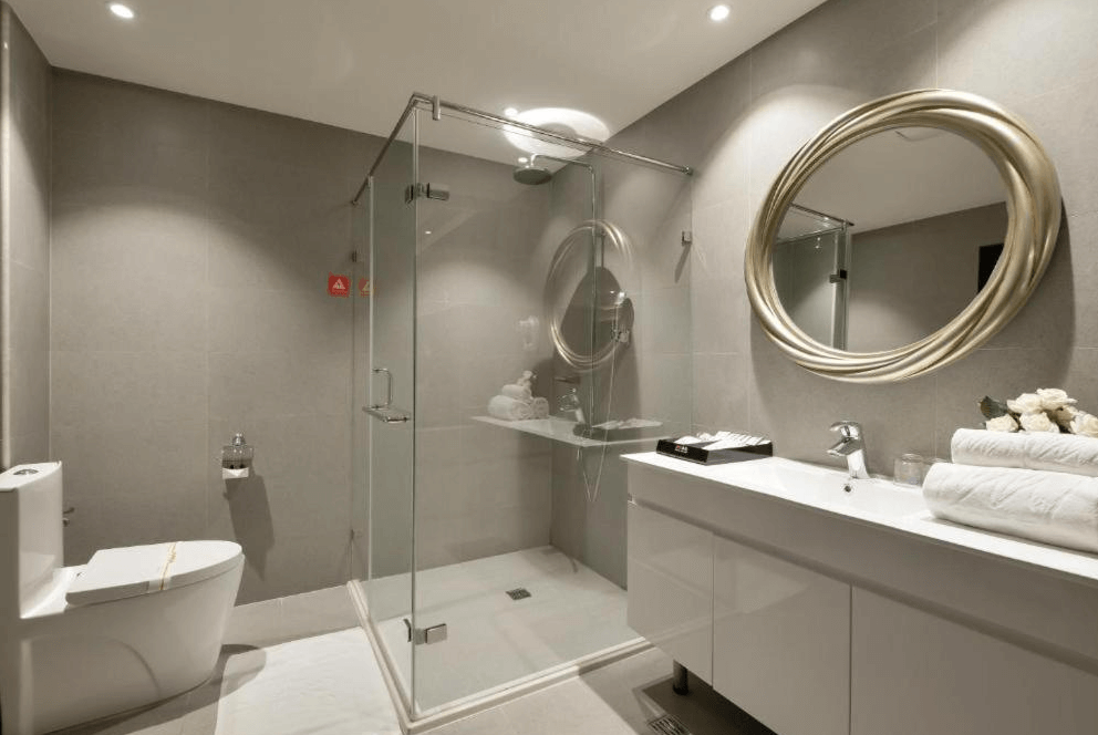 【草屯住宿】沐悅時尚精品旅館的現代衛浴，設有獨立玻璃淋浴間、圓形設計鏡面與寬敞洗手台，牆面與地板為淺灰色磁磚，整體簡潔明亮，乾濕分離設計方便又衛生。