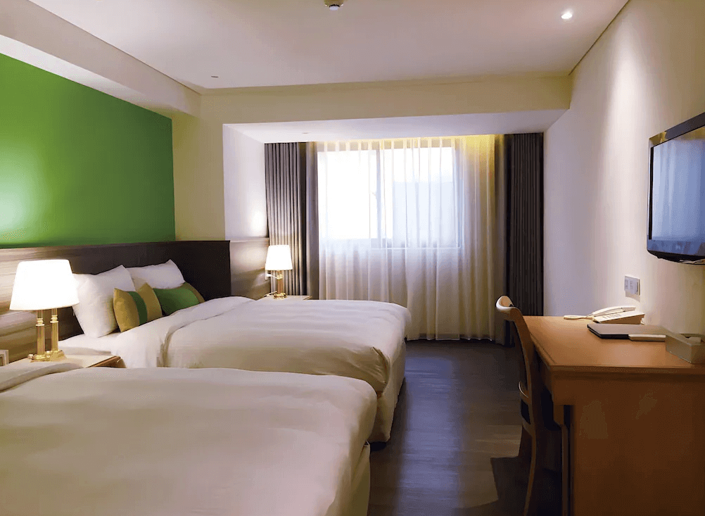 【台北小巨蛋住宿】洛碁大飯店三貝茲的家庭房，配置兩張大床與木質書桌，融合綠色牆面與柔和燈光，提供舒適的親子或團體住宿空間。