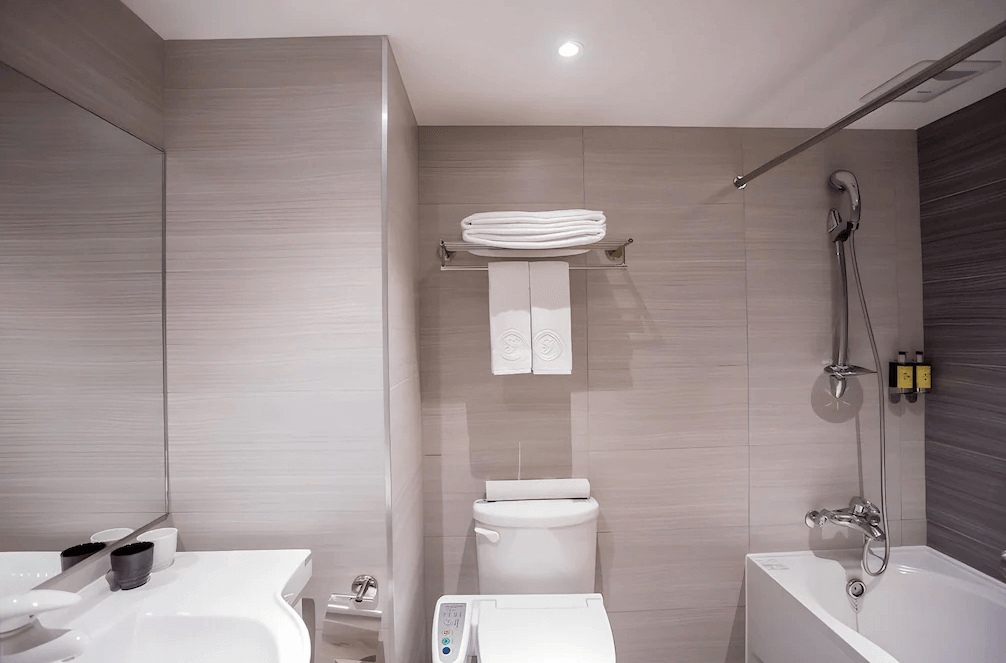 【台北小巨蛋住宿】洛碁大飯店三貝茲的浴室設計，搭配免治馬桶、浴缸與淋浴設備，牆面採用淡灰色磁磚，營造清新質感氛圍。