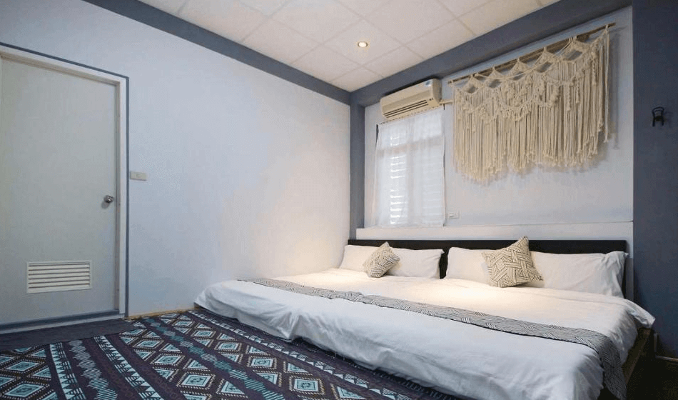 【綠島住宿】海島旅人的三人房，設有加大雙人床與加床，牆面以手工編織掛飾點綴，地面鋪設幾何圖案地毯，營造出溫暖的休憩氛圍。