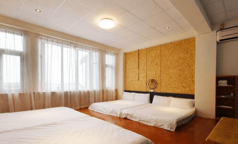 【綠島住宿】海島旅人的四人家庭房，兩張雙人床配置於木地板空間，大片落地窗搭配白色紗簾，引入自然光線，牆面以木質裝飾增添質感。