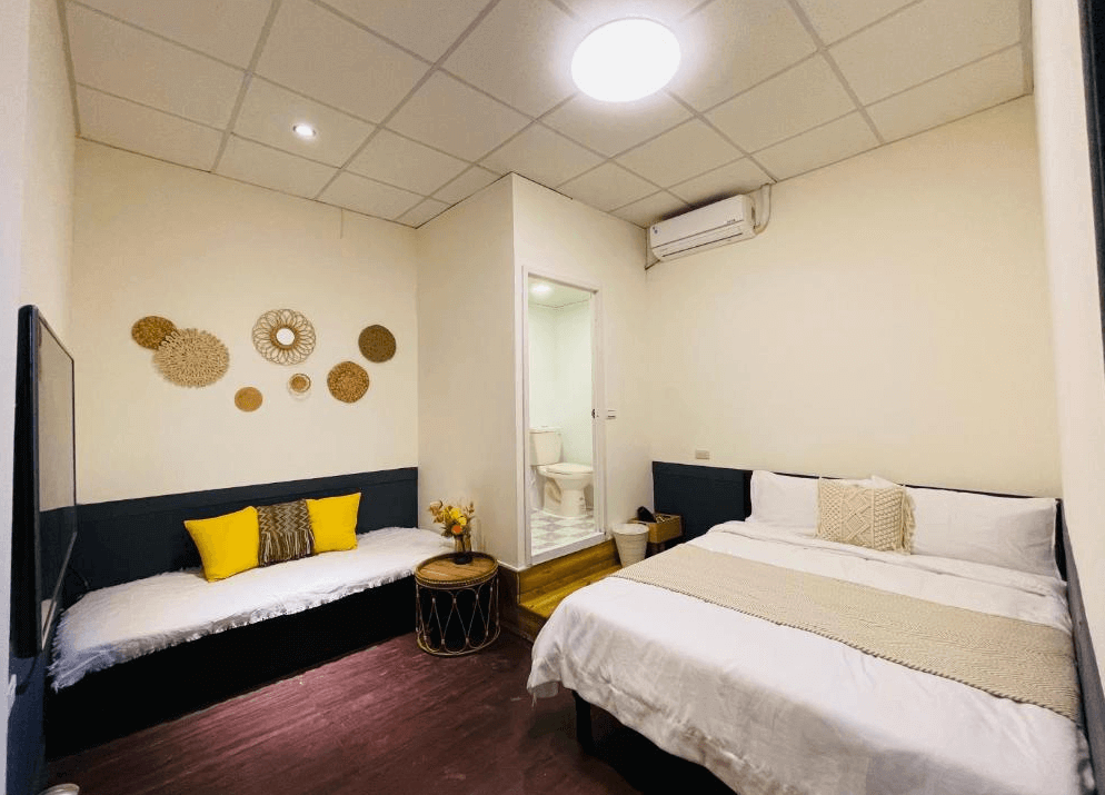 【綠島住宿】海島旅人的雙人房設有一張雙人床與一張沙發床，牆面點綴有編織風掛飾與黃色抱枕，附設獨立衛浴，適合小家庭或情侶入住。