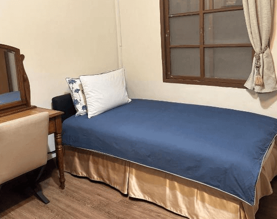 【左營住宿】海軍官邸四號院單人房空間，以簡潔設計為主，配有深藍床罩單人床與復古梳妝台，窗邊有木框窗戶與淺色窗簾，溫馨舒適。