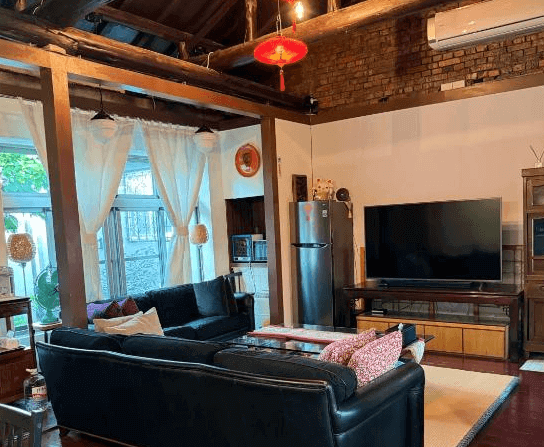 【左營住宿】海軍官邸四號院復古風格客廳空間，融合木造結構與現代家電，配有黑色沙發、大片電視與冰箱，挑高設計與磚牆呈現濃厚復古氛圍。