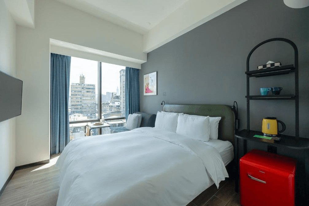 【台北寵物友善住宿】瀚寓夏天的雙人房，配有一張舒適雙人床、大片落地窗與城市景觀，牆面為灰白對比設計，房內設有紅色小冰箱與黑色層架，搭配亮黃色快煮壺與馬克杯，氣氛輕鬆活潑。