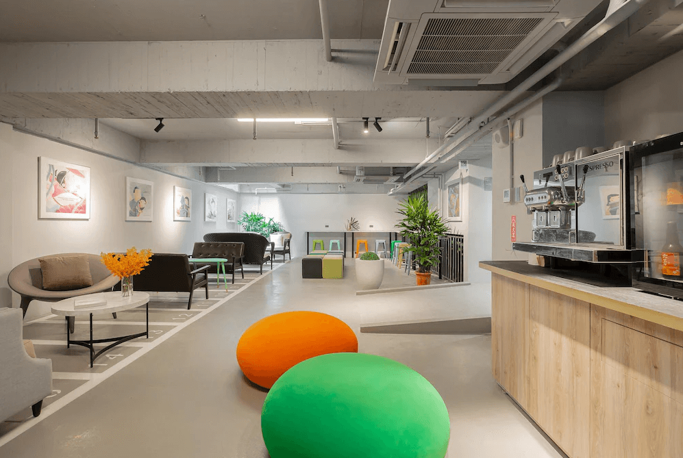 【台北寵物友善住宿】瀚寓夏天的交誼空間，配置多樣座位與沙發，地板繪有跳格子圖案，放置彩色軟墊與藝術掛畫，右側設有自助咖啡吧，整體氣氛輕鬆自在，適合交流與休憩。