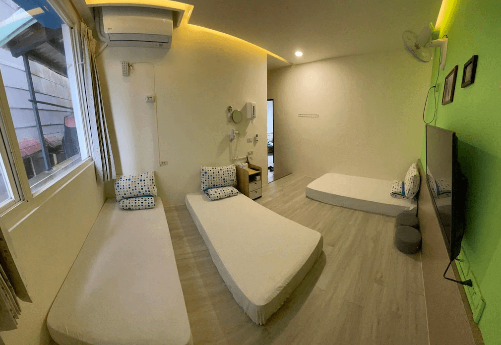 【綠島住宿】火燒島潛水度假中心的多人通舖房型，設有三張單人床墊與電視，牆面以淡綠色與米色為主，空間明亮通風，適合潛水客或小團體入住。