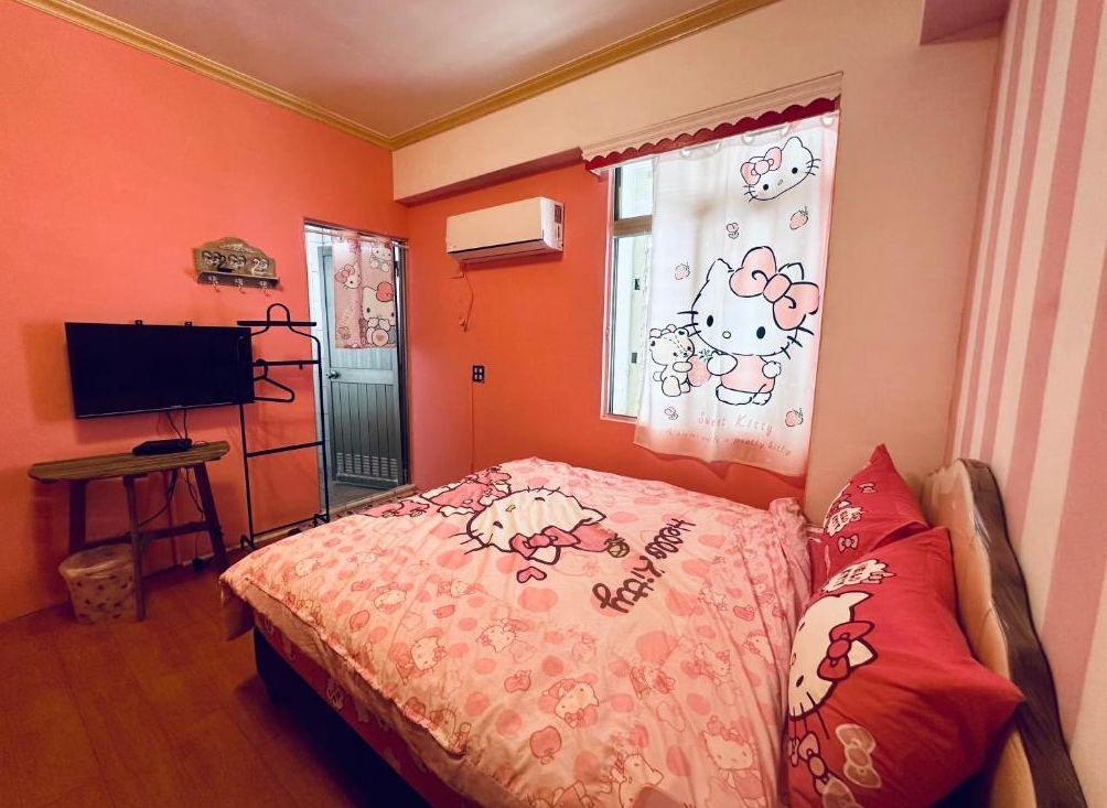 【綠島寵物友善住宿】燈光夏的粉紅色系牆面與Hello Kitty主題寢具布置的雙人房，房內設有電視、冷氣與衣架，窗簾與床組皆印有可愛的Hello Kitty圖案，呈現溫馨童趣風格。