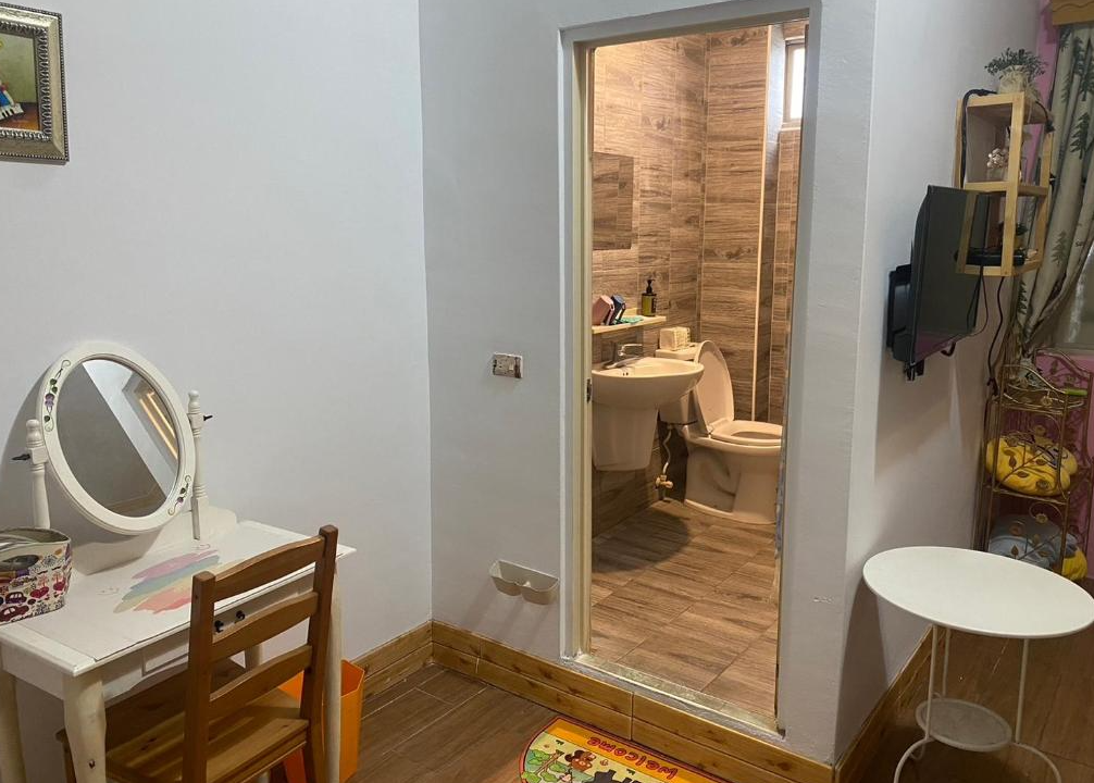 【綠島寵物友善住宿】燈光夏房內附設木紋磁磚的獨立衛浴空間，旁邊有一組白色梳妝台與小椅子，簡潔實用的設計提供便利的住宿體驗。