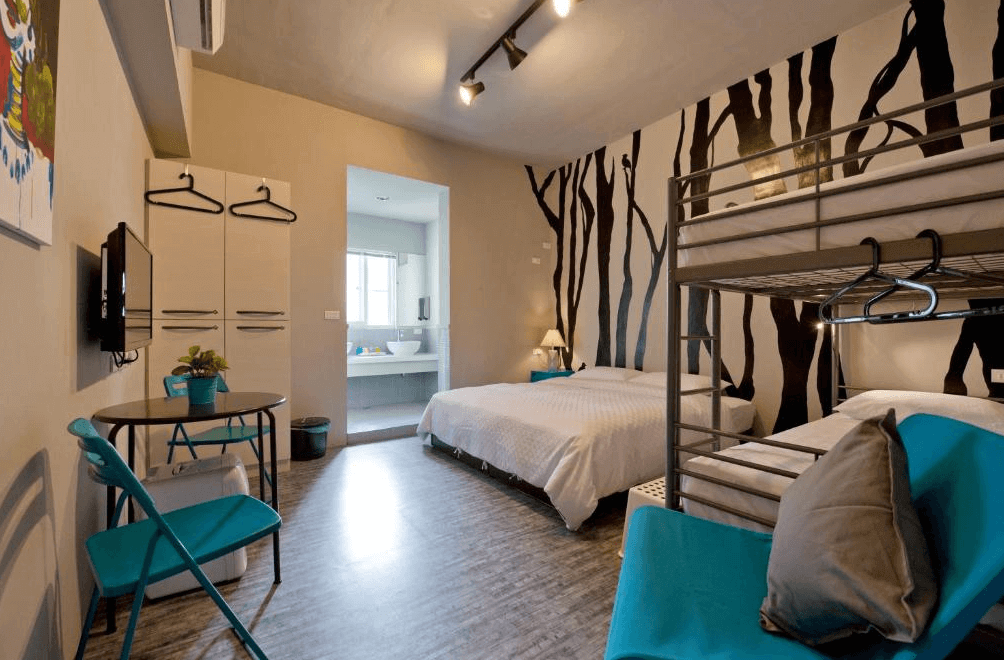 【左營住宿】理歐111民宿的房間牆面以黑色樹林圖案設計，設有雙人床與上下鋪床型，搭配藍綠色座椅與簡約家具，風格活潑現代，適合親子入住。