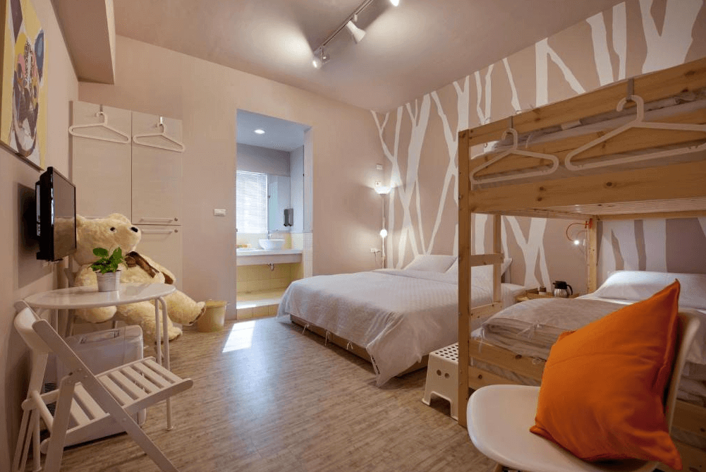 【左營住宿】理歐111民宿的房內配有雙人床與木製上下鋪，牆面為白色森林圖騰設計，擺放有大型玩偶與橘色抱枕，營造溫暖童趣氛圍。