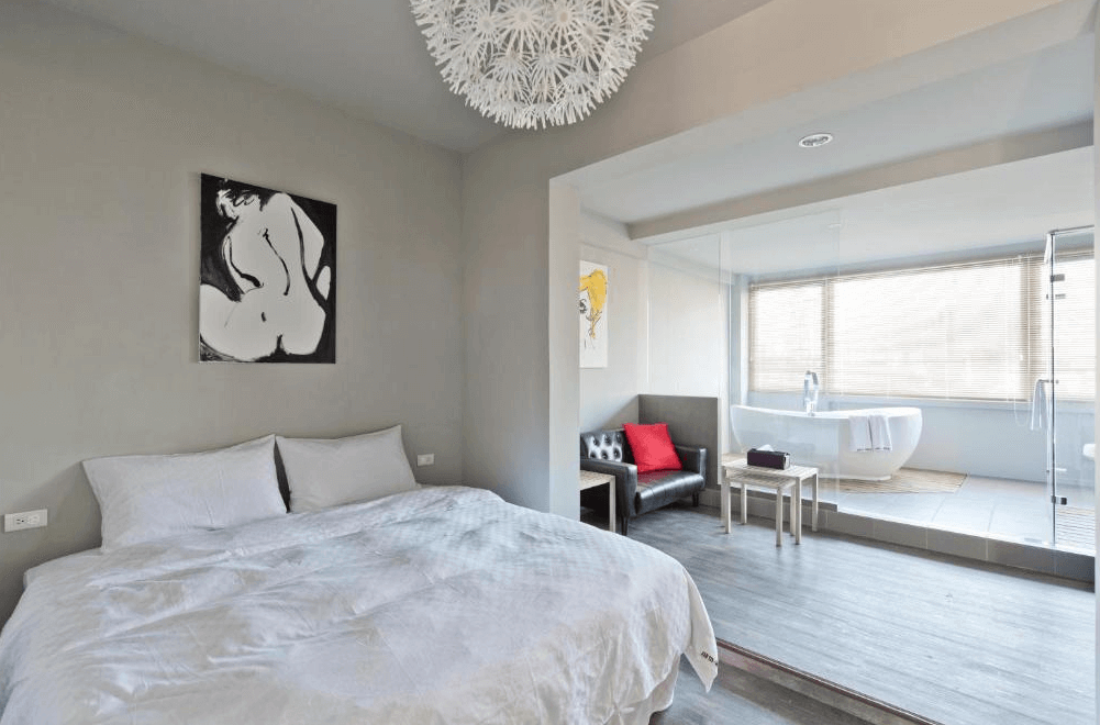 【左營住宿】理歐111民宿的房間設計簡潔大方，以灰白色為主色調，設有雙人床、黑色沙發與開放式浴缸區，大片玻璃窗提供明亮採光。