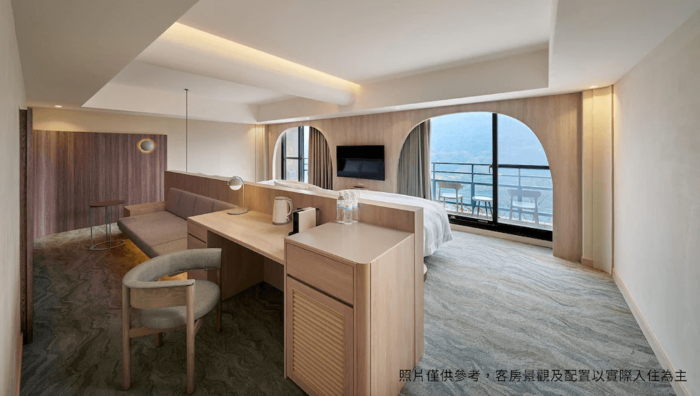 【龍潭住宿】石門水庫福華渡假飯店的家庭房型，前方設有辦公桌與沙發休憩區，後方為景觀床區，可直接眺望湖景或山景。設計簡潔流暢，以柔和曲線及大面窗戶帶出自然光線與視野，適合親子或長住旅客。