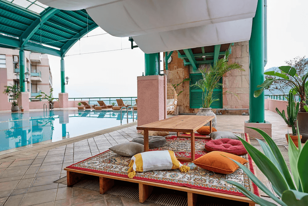 【龍潭住宿】石門水庫福華渡假飯店，頂樓露天泳池空間設有遮陽棚與躺椅，旁邊鋪設波西米亞風格地毯與彩色靠墊、抱枕，提供悠閒的發呆平台與拍照打卡角落。整體空間綠植點綴，兼具度假風與放鬆感。