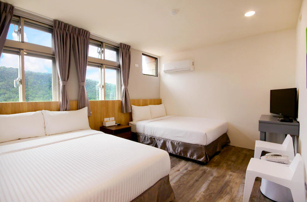 【綠島寵物友善住宿】綠島 統祥大飯店的四人房，房內配有兩張雙人床，木質地板與柔和的窗簾營造舒適氛圍，窗外可見青翠山景，自然採光明亮，空間寬敞整潔。