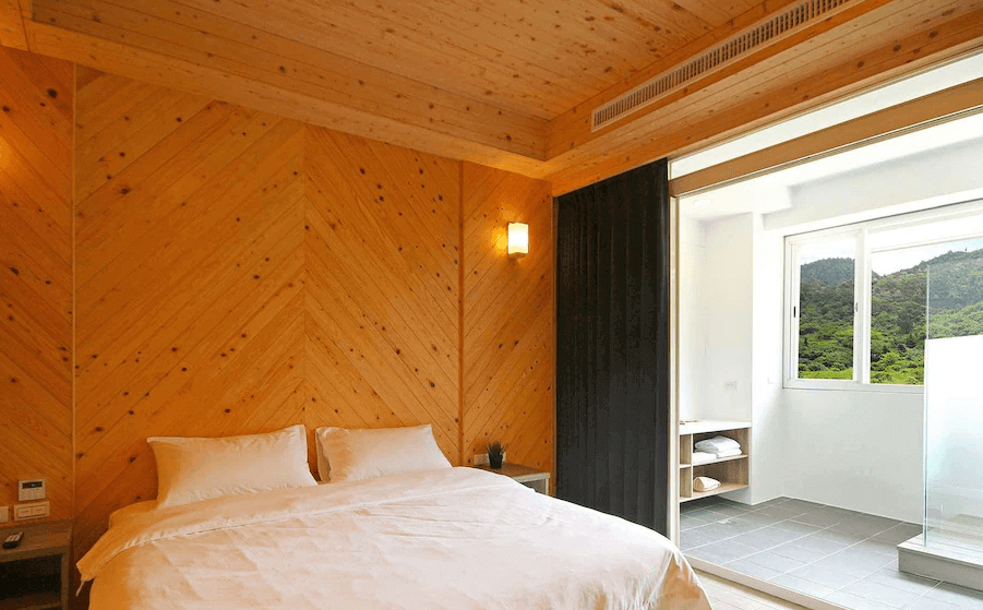 【綠島住宿】綠島House16的雙人房，牆面與天花板皆採木紋斜紋拼接，營造溫潤自然氛圍，大片落地窗外可欣賞翠綠山景與開放式陽台空間。
