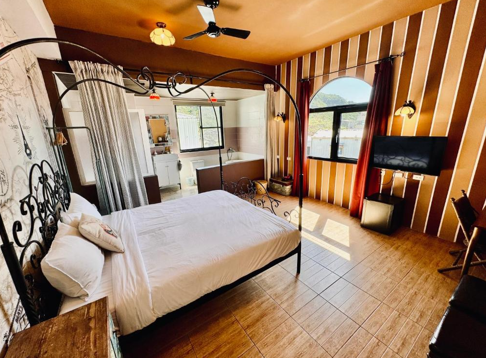 【綠島寵物友善住宿】綠島寧靜海潛水-城堡館的歐式風情雙人房空間，配置有華麗鐵藝床架與木質地板，房內設有大片窗戶引入自然光，浴室與臥室以拉簾隔開，整體氛圍溫馨典雅。