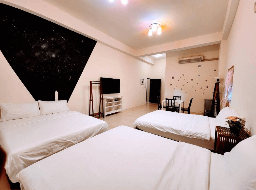 【綠島住宿】綠島彩虹民宿的四人房設有兩張雙人床，牆面以黑色幾何圖形與星空圖樣裝飾，配備電視、用餐桌與冷氣，整體風格簡約中帶點創意感。