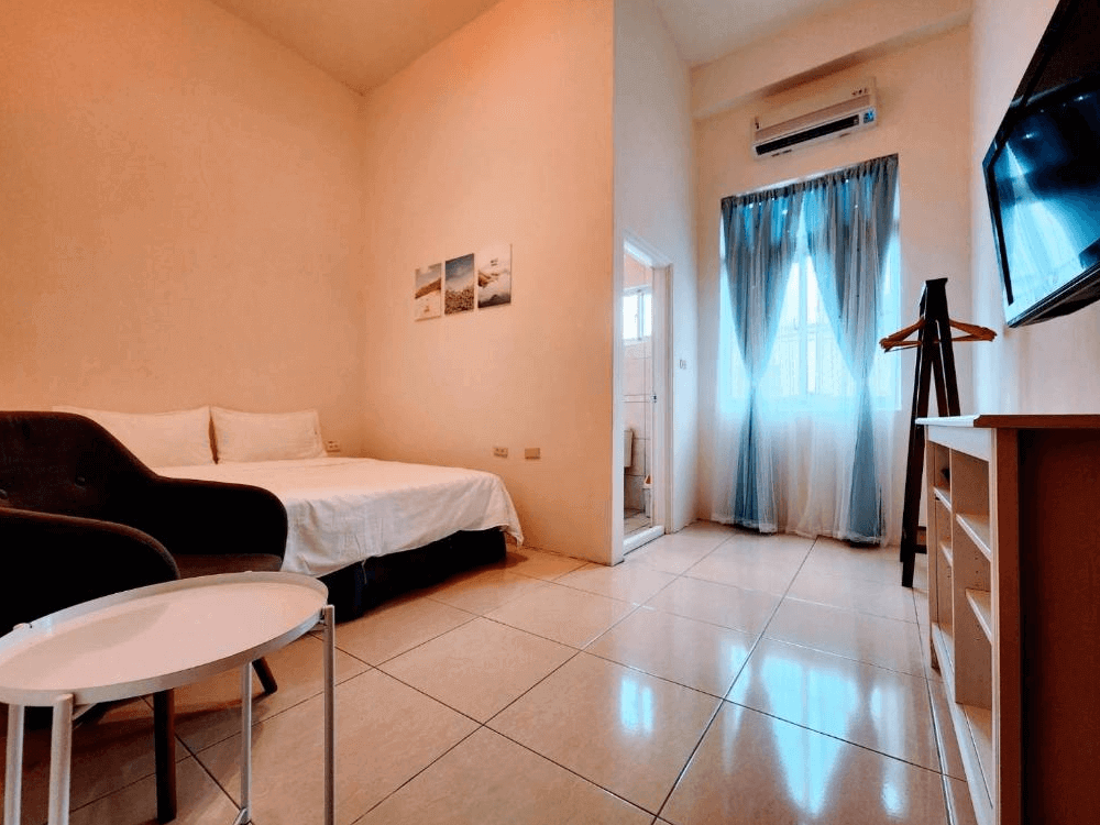 【綠島住宿】綠島彩虹民宿的雙人房，設有雙人床、沙發椅與電視，大片落地窗搭配藍白紗簾，自然光充足，附設獨立衛浴空間，環境簡潔舒適。