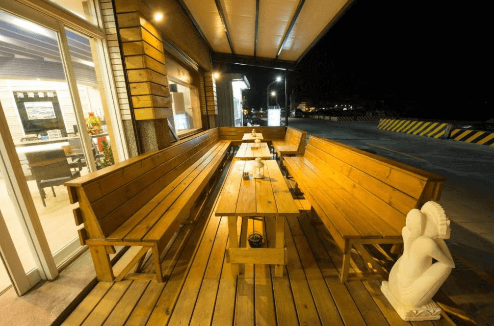 【綠島住宿】綠島海灣會館的戶外露天木製座位區，設有長形木桌與長椅，靠近臨海道路，氣氛溫馨悠閒，適合旅人交流與享受海風。