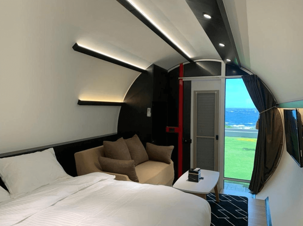 【綠島住宿】綠島涵館TUBE18的海景客房，設有舒適雙人床與沙發，天花板採流線型設計，牆面燈光柔和，窗外可直接欣賞遼闊草地與湛藍大海。