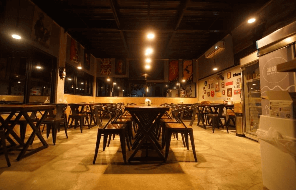 【綠島住宿】綠島涵館TUBE18的公共用餐區空間寬敞，木製桌椅排列整齊，牆面掛有各式旗幟與藝術裝飾，燈光溫暖營造出濃厚的工業風格氛圍。