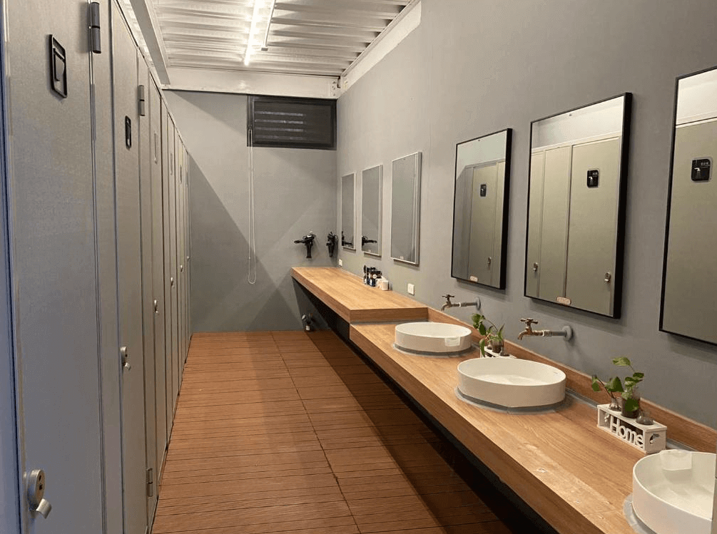 【綠島住宿】綠島涵館TUBE18的共用衛浴空間，配備獨立洗手台、鏡子與乾濕分離淋浴間，設計簡潔整潔，木質地板與綠色植栽增添溫馨感。