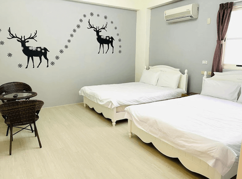 【綠島住宿】綠島藍漾海墅的四人房，以白灰色調為主，牆面上裝飾有黑色麋鹿圖案與雪花貼紙，兩張典雅雕花床架搭配編織桌椅，展現溫暖典雅的氛圍。