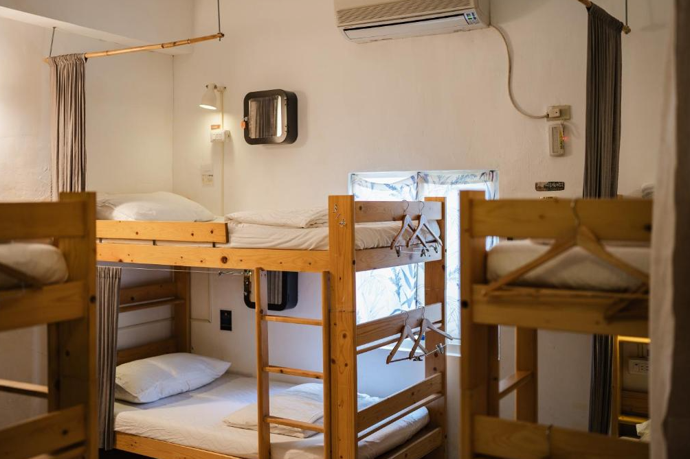 【綠島寵物友善住宿】"綠島住宿"緩島旅宿的多人背包客房，木製上下舖整齊排列，每個床位附有掛衣架與簾幕，房內配有冷氣、閱讀燈與小窗戶，自然光灑入營造溫馨氛圍。