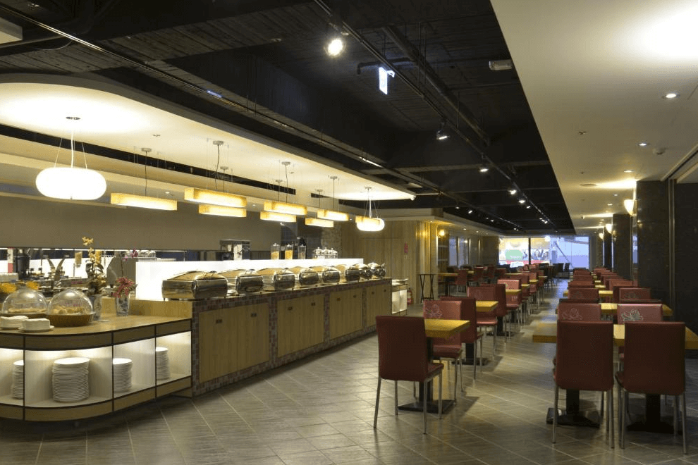 【草屯住宿】草屯福美大飯店的自助餐廳，設有長型自助吧檯與整齊排列的紅色座椅與木質桌椅，燈光柔和、空間寬敞，提供多樣化餐點選擇，是用餐與聚會的舒適空間。