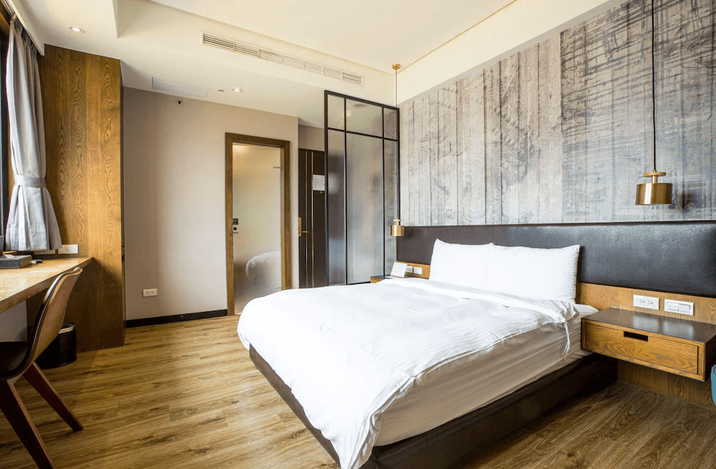 【一中街住宿】葉綠宿一中館的雙人房，木質地板搭配灰色仿清水模牆面，床頭吊燈營造現代風格氛圍，大片窗戶引進自然光，設有簡約木質書桌與舒適空間。