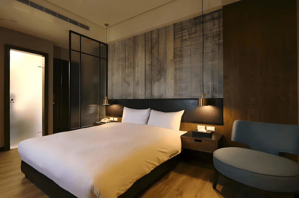 【一中街住宿】葉綠宿一中館的雙人房夜景，床頭牆面以灰木紋與燈光投射層次感，搭配現代吊燈與低調家具，營造安靜放鬆的住宿氛圍。