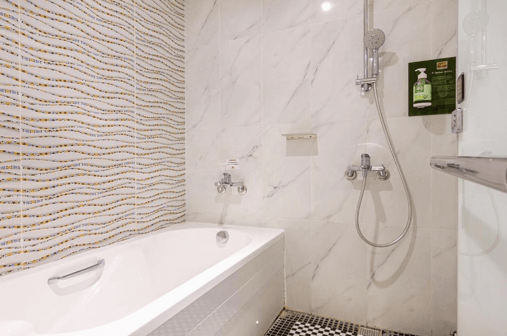 【蘆洲住宿】雀客旅館-新北蘆洲的衛浴空間配有白色浴缸與手持蓮蓬頭，牆面為大理石花紋磚與波浪形馬賽克磁磚組合，設計感十足。備有洗髮精與沐浴用品，乾淨明亮、機能齊全。