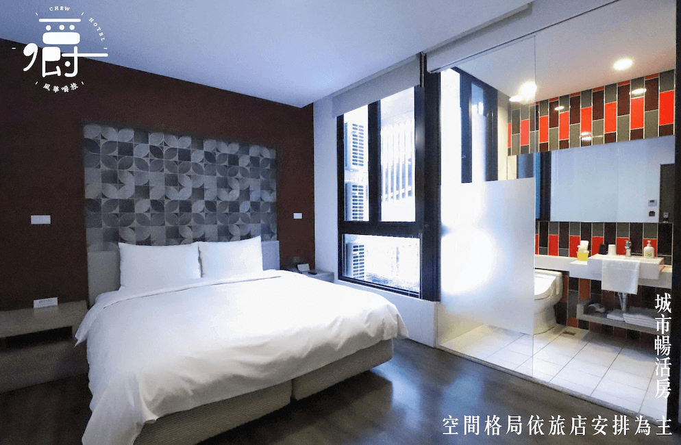 【一中街住宿】風華嚼旅的雙人房，配有一張雙人床與幾何圖案床頭設計，大片窗景引入自然光，浴室採半開放式設計並以紅黑磁磚裝飾，視覺感十足。