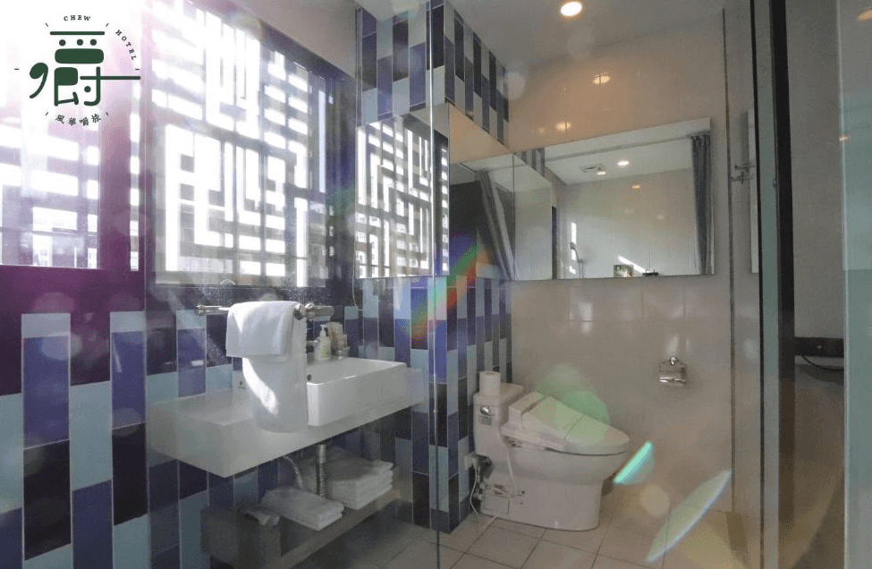 【一中街住宿】風華嚼旅的浴室設計亮眼，牆面採用紫藍色系磁磚拼貼，搭配大片對外窗引入自然光，設有免治馬桶與簡約洗手台，光線通透、整潔明亮。