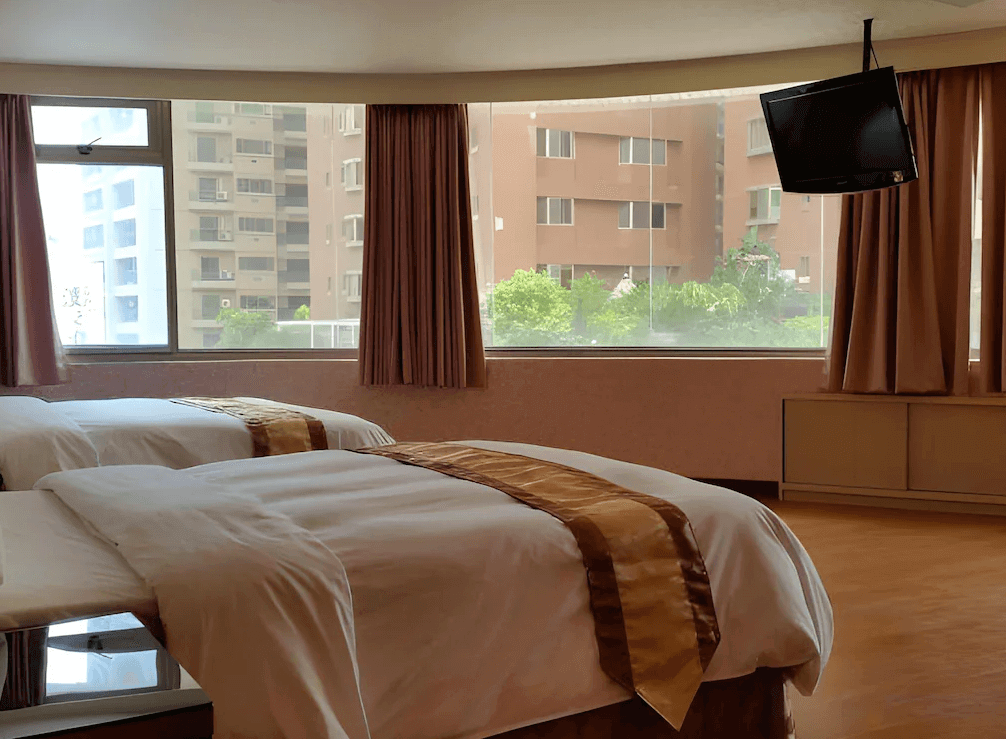 【左營住宿】龍翔大飯店的房內設有大片落地窗，可俯瞰城市街景，兩張床整齊擺放，窗簾為柔和米色調，搭配壁掛式電視。