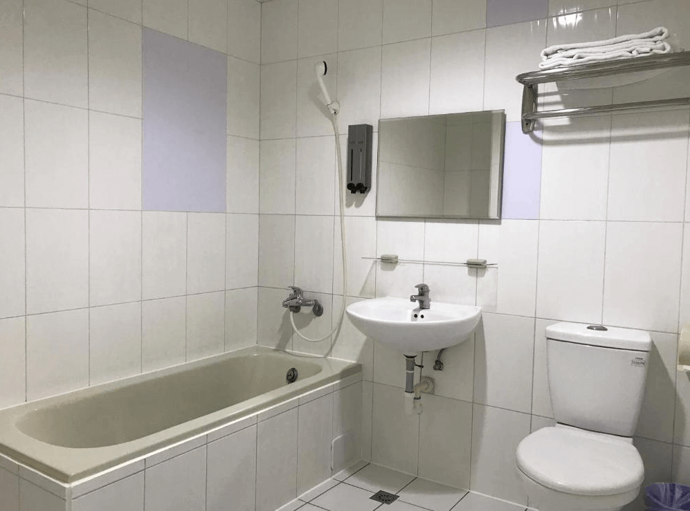 【左營住宿】龍翔大飯店的浴室以白色磁磚為主，配有浴缸、淋浴設備、洗手台與馬桶，牆上附有毛巾架與鏡子，設計簡潔實用。