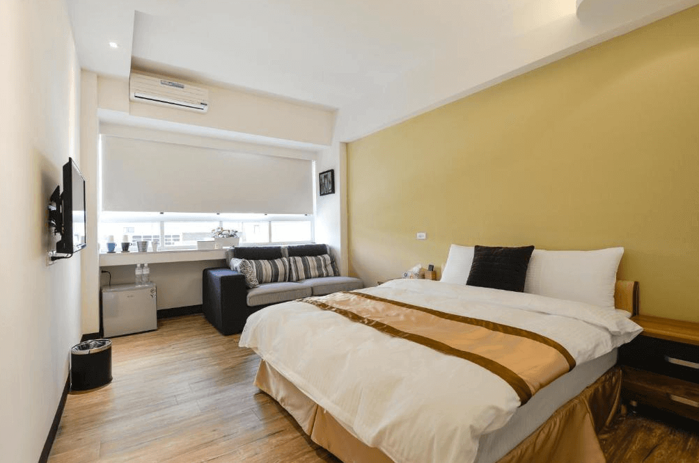 【高雄寵物友善住宿】237重機主題旅店的雙人房，配有一張大床、柔和的黃色牆面與木質地板，窗邊設有沙發與小冰箱，整體風格溫馨實用，適合情侶或旅人休憩。
