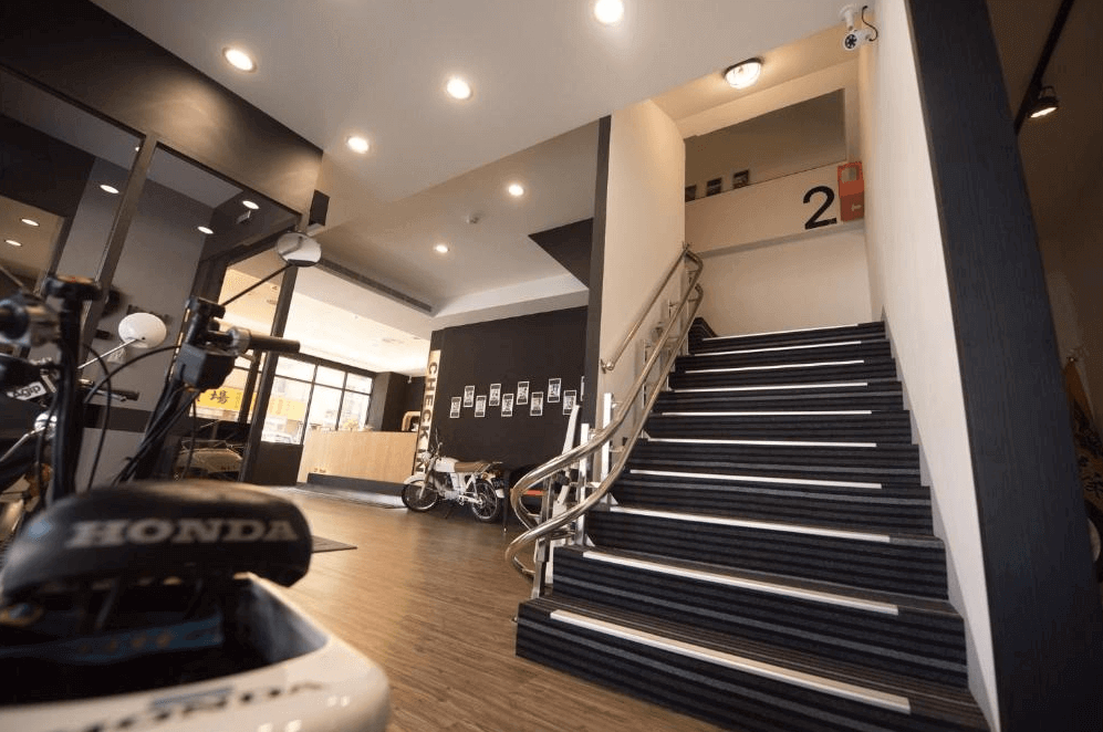 【高雄寵物友善住宿】237重機主題旅店的接待區結合重機主題風格，牆上掛有裝飾相片，樓梯與設計線條具現代感，地板為木紋質感，空間擺放數輛摩托車，展現濃厚重機文化氛圍。